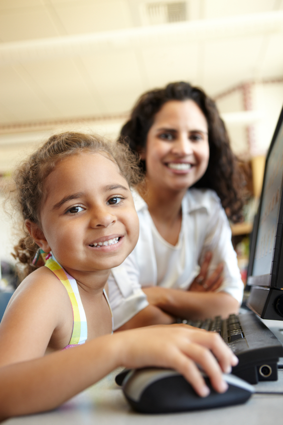 smiling student using computer with teacher