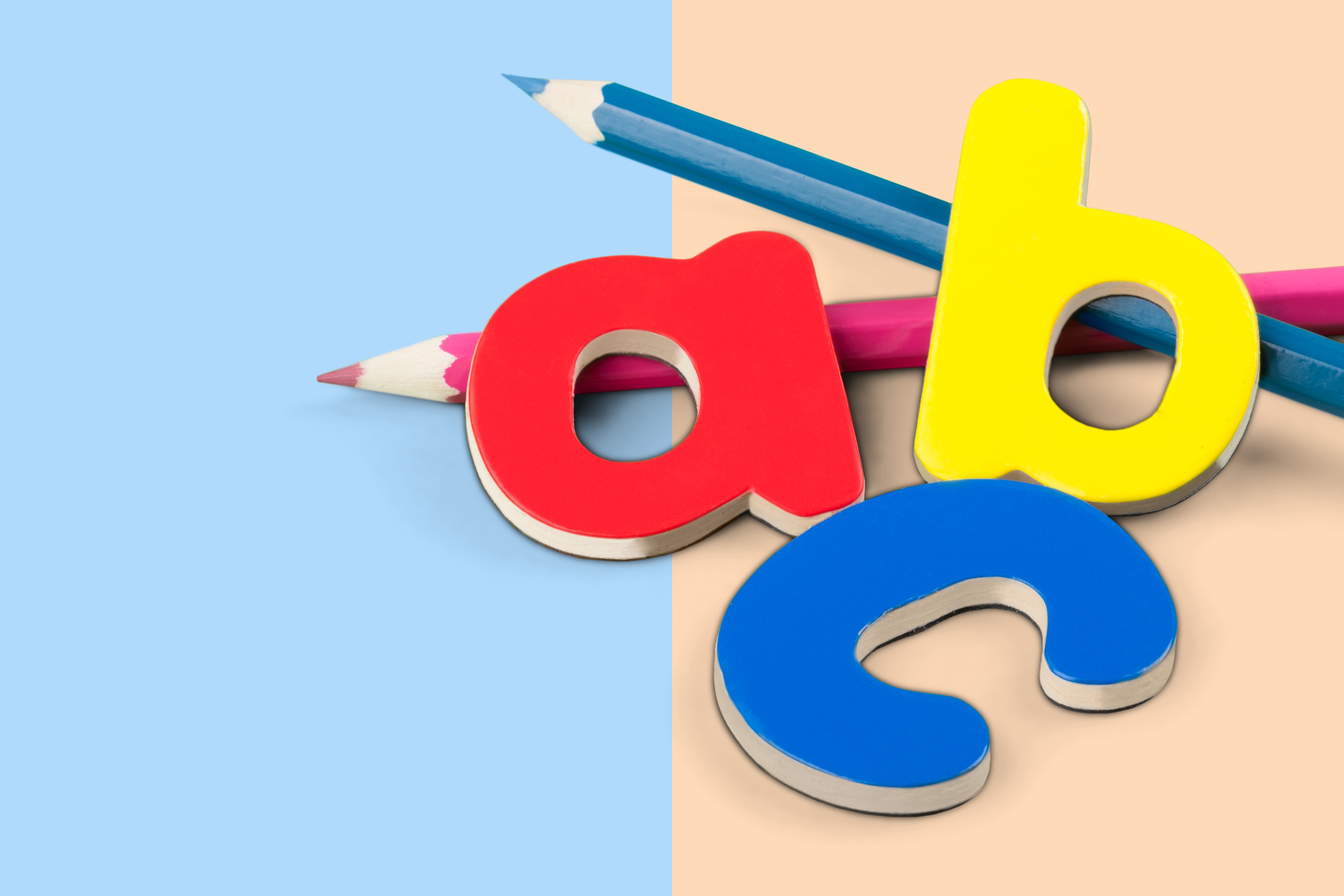 Colorful wooden letters A, B, and C with pink and blue pencils on a pastel split background.