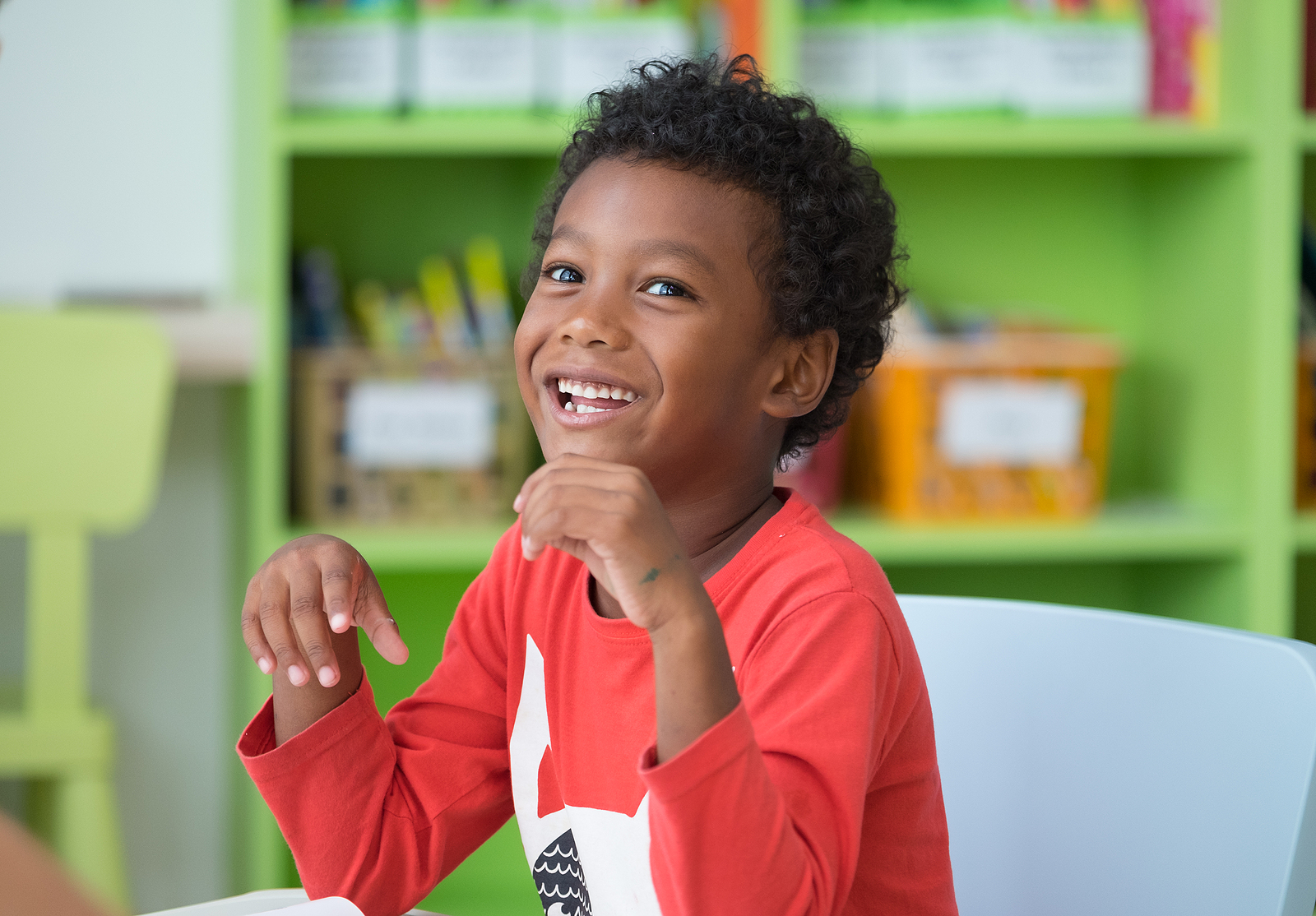 Smiling young student in a colorful classroom, engaged in a learning activity as part of a special education reading program.