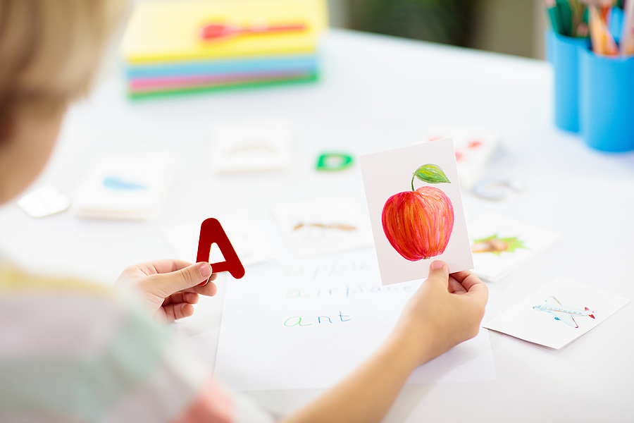 Child practicing phonics by matching the letter A with a picture of an apple during a phonics reading activity.