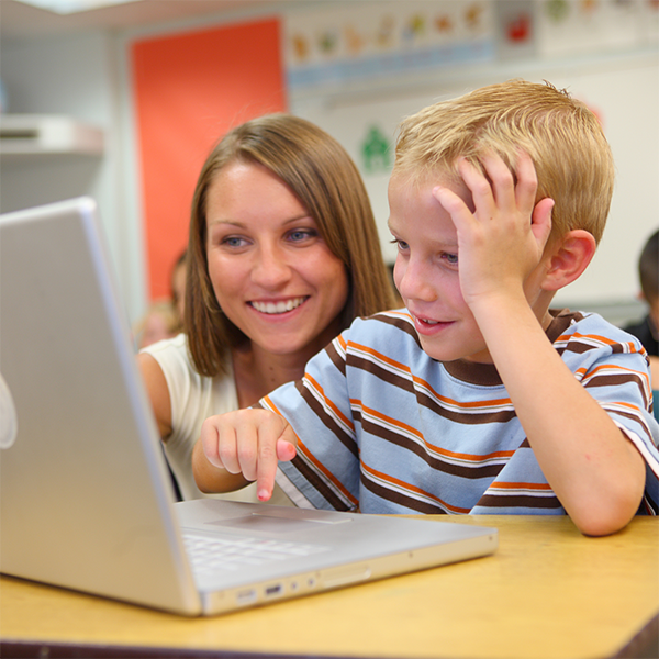 Teacher helping elementary student build math fluency through online math facts practice on a laptop.
